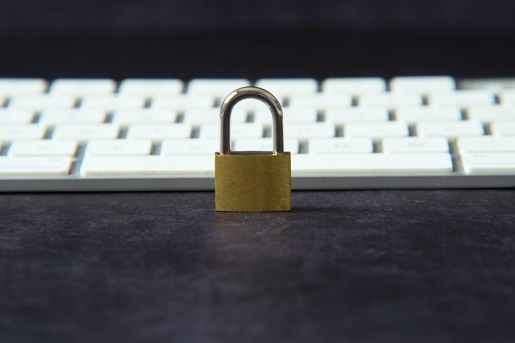 A sturdy padlock sits on a black table in front of a computer keyboard.