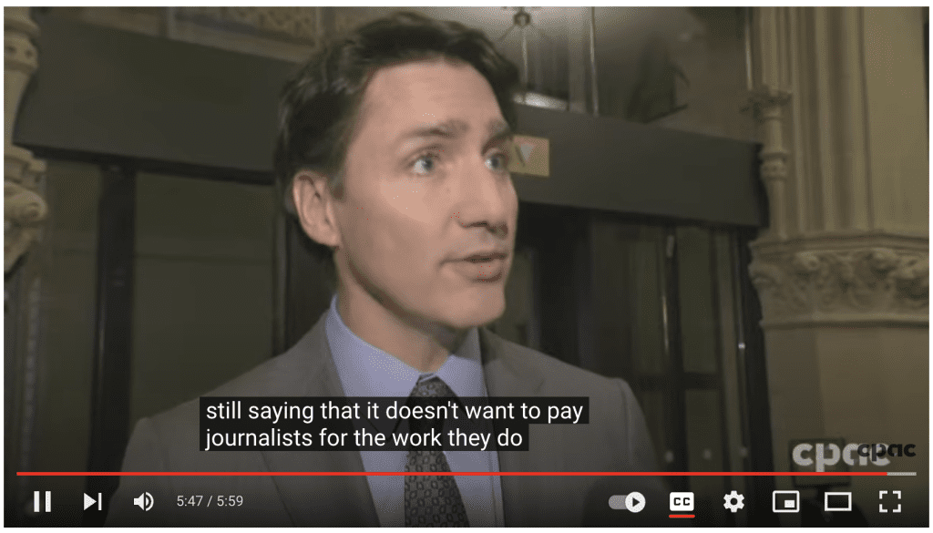 Video shot of Trudeau with the closed caption 'still saying that it doesn't want to pay journalists for the work they do'.