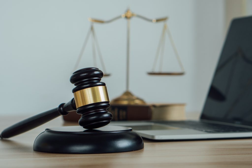 Scales and a computer laptop form the background for a judge’s gavel on a desk.