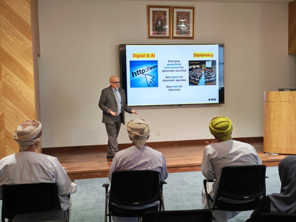  People, Person, Crowd, Adult, Male, Man, Female, Woman, Chair, Furniture, Clothing, Hat, Art, Painting, Electronics, Screen, Audience, Projection Screen, Accessories, Glasses, Architecture, Building, Classroom, Indoors, Room, School, Footwear, Shoe, Formal Wear, Tie, Lecture, Seminar, Computer Hardware, Hardware, Monitor, Coat, Speech