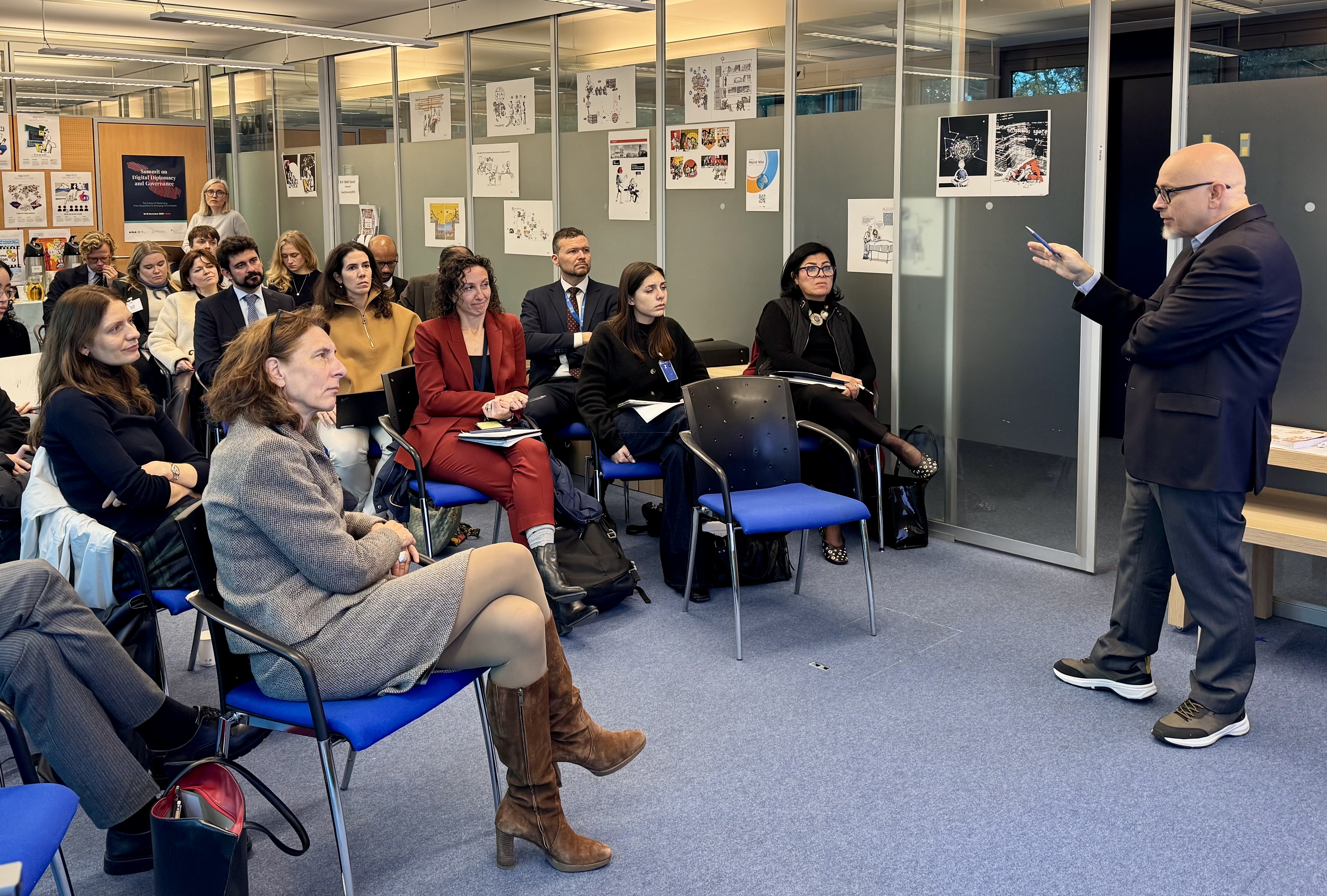 IMG_4123 Adult, Female, Person, Woman, Clothing, Footwear, Shoe, Crowd, Accessories, Bag, Handbag, Chair, Furniture, Male, Man, Glasses, Audience, Indoors, Wristwatch, Electronics, Mobile Phone, Phone, Speech, Formal Wear, Suit, Lamp, Sandal, Jewelry, Necklace, Ralf König, Alexis Georgoulis, Cyrille Diabaté, Oleg Kononenko, Jolyon Palmer, Claude Chirac