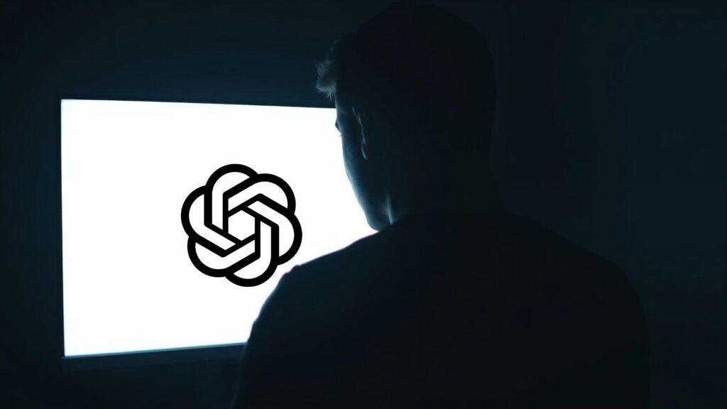 Silhouette of a person facing a glowing screen displaying the OpenAI logo, symbolising ChatGPT misuse in disinformation and scam campaigns