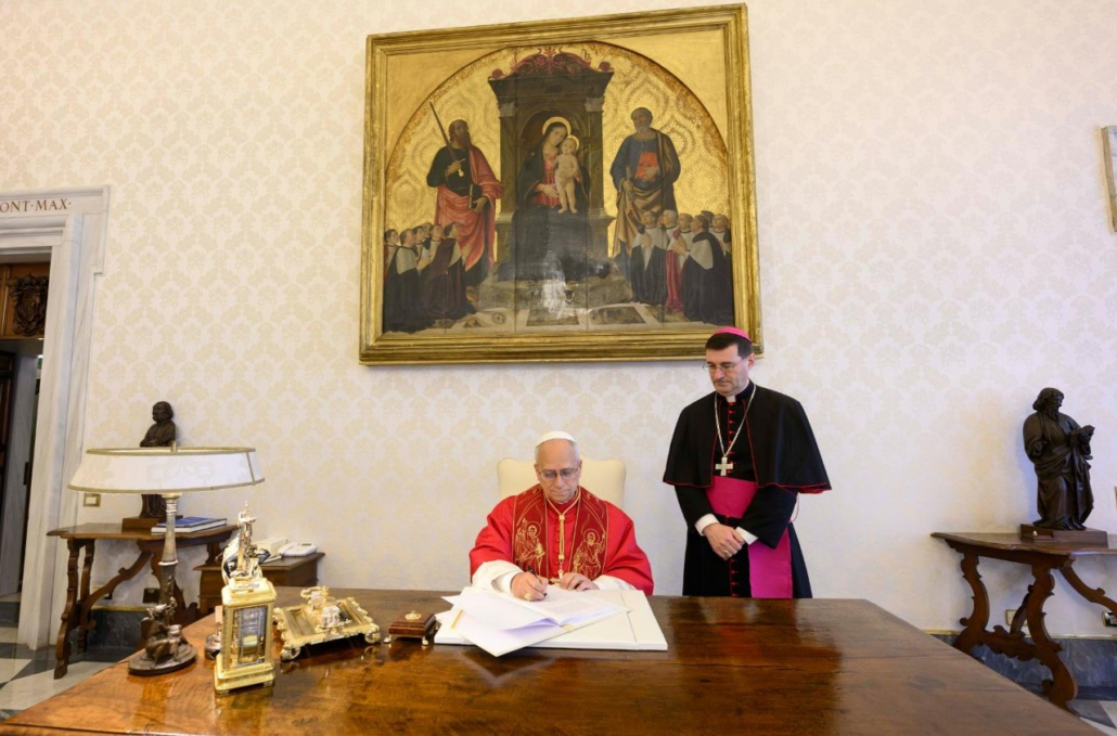 The image shows a photography of Pope Leo XIV signing a document