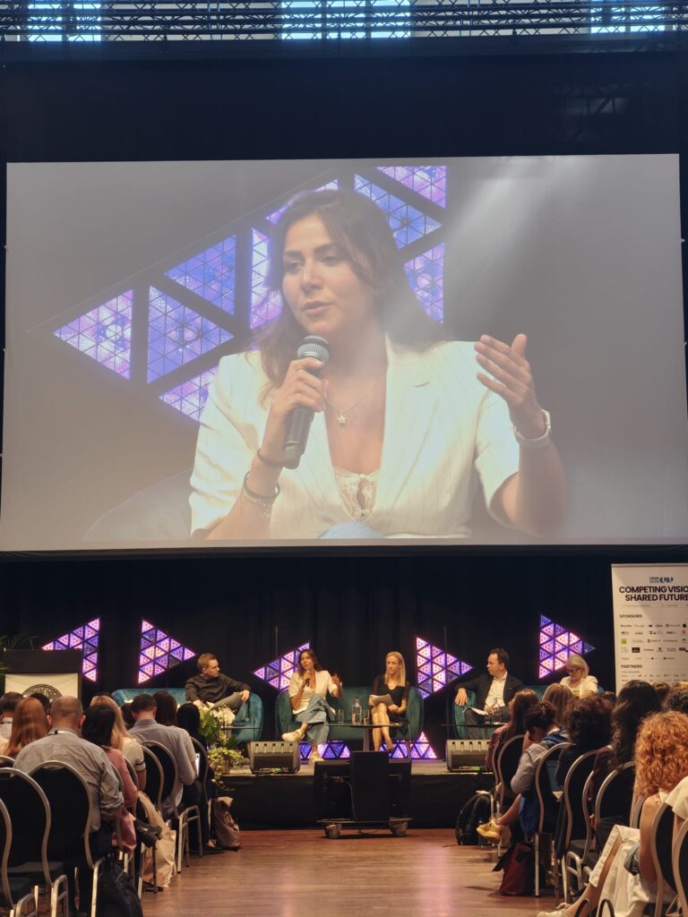 Europe's digital crossroads: Key takeaways from CPDP 2026 2 People, Person, Crowd, Adult, Female, Woman, Electrical Device, Microphone, Accessories, Bag, Handbag, Audience, Jewelry, Necklace, Electronics, Speaker, Male, Man, Clothing, Footwear, Shoe, Indoors, Speech, Carrie Vaughn, Vian Dakhil